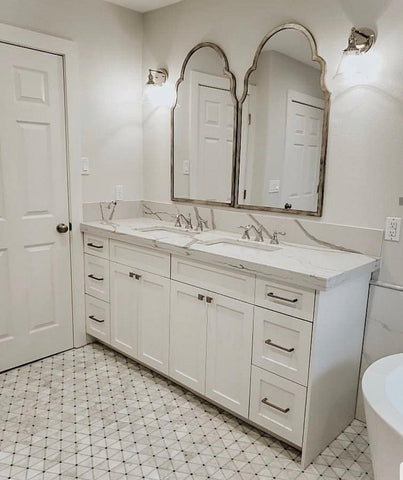White, modern bathroom cabinets and fixtures sit on light, marble triangle mosaic tile