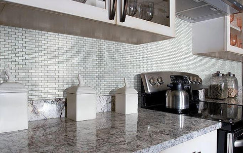 Marble countertops and silver stove against mini brick mosaic tile wall in kitchen