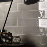 4x16 Gioia Greige color tile stagger set on a wall behind a table with lamp and other objects.