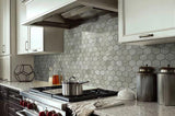 Kitchen with gray hexagonal tile accent wall, marble countertops, stovetop and white cabinets