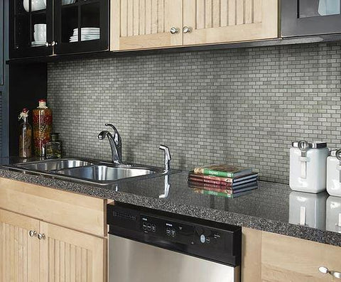 Dark kitchen countertops and birch cabinets against limestone tile wall in mini brick mosaic